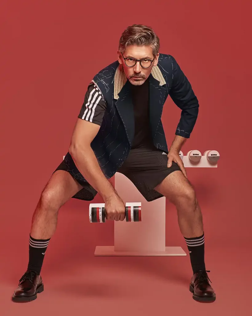 fotografia de jose manuel del estudio de arquitectura Estudi{h}ac posando con los galardones que ha diseñado para room con Krion, en una escena de imitación de haciendo deporte en fondo rojo
