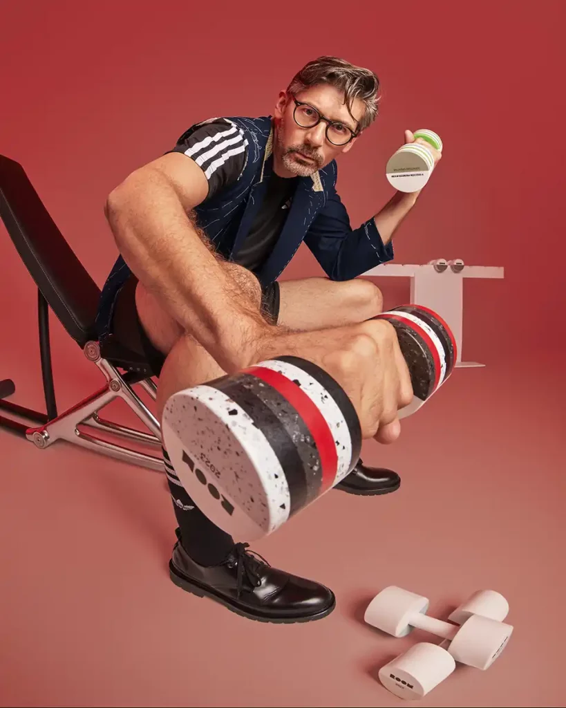fotografia de jose manuel del estudio de arquitectura Estudi{h}ac posando con los galardones que ha diseñado para room con Krion, en una escena de imitación de haciendo deporte en fondo rojo