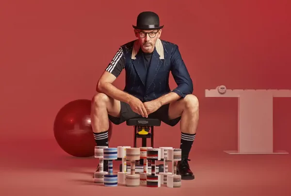 fotografia de jose manuel del estudio de arquitectura Estudi{h}ac posando con los galardones que ha diseñado para room con Krion, en una escena de imitación de haciendo deporte en fondo rojo