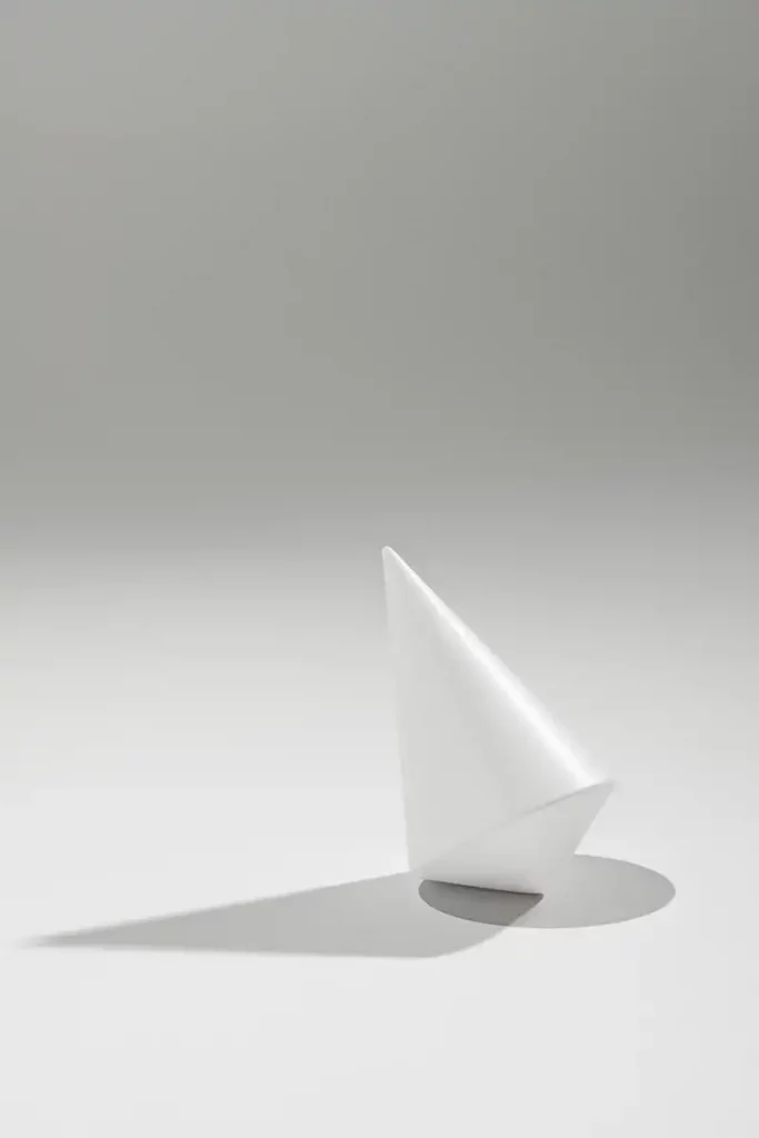 Bodegón de fotografía de producto comercial mostrando varios galardones en forma de peonza para los Premios ROOM. Los trofeos, fabricados en Krion blanco hielo, descansan sobre un fondo neutro y destacan por sus finas líneas grabadas en distintos colores flúor como rojo, azul y amarillo, con el logotipo de la revista sutilmente integrado.